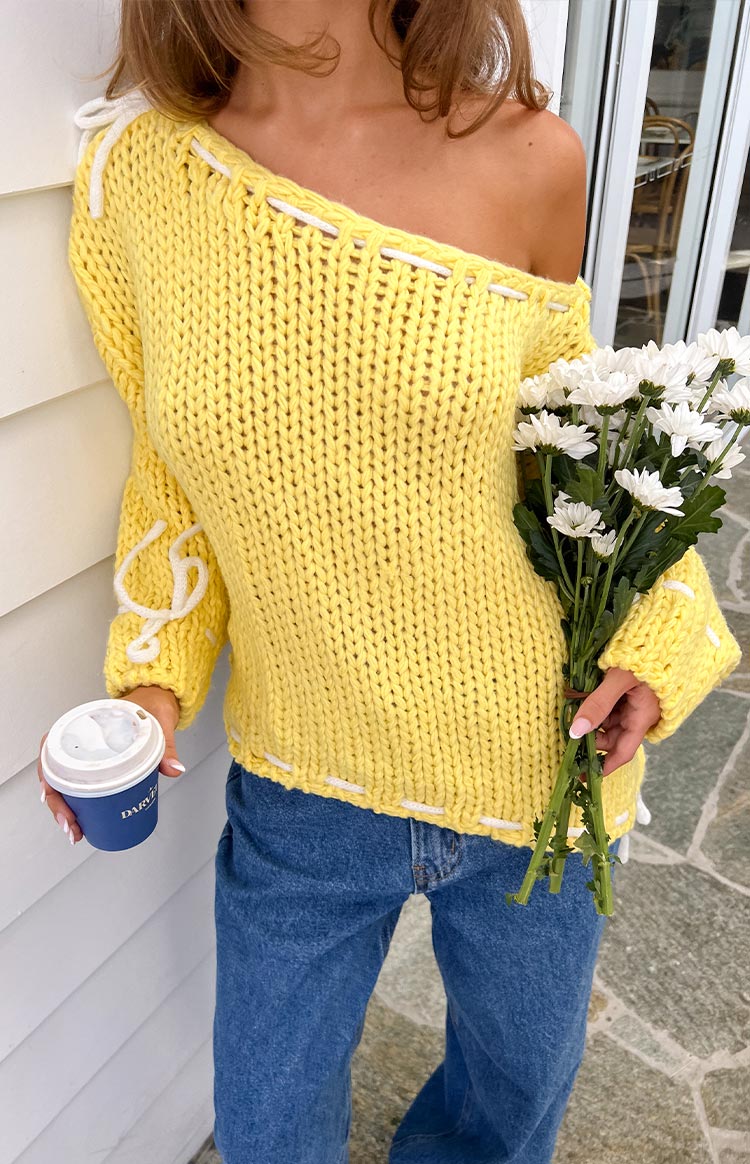 Yellow chunky knit sweater with white lacing detail on the off-shoulder neckline, cuffs, and bottom hem