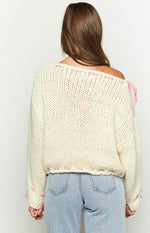 Rear view of a cream chunky knit sweater with pink ribbon lacing along the off-shoulder neckline, hem, and cuffs