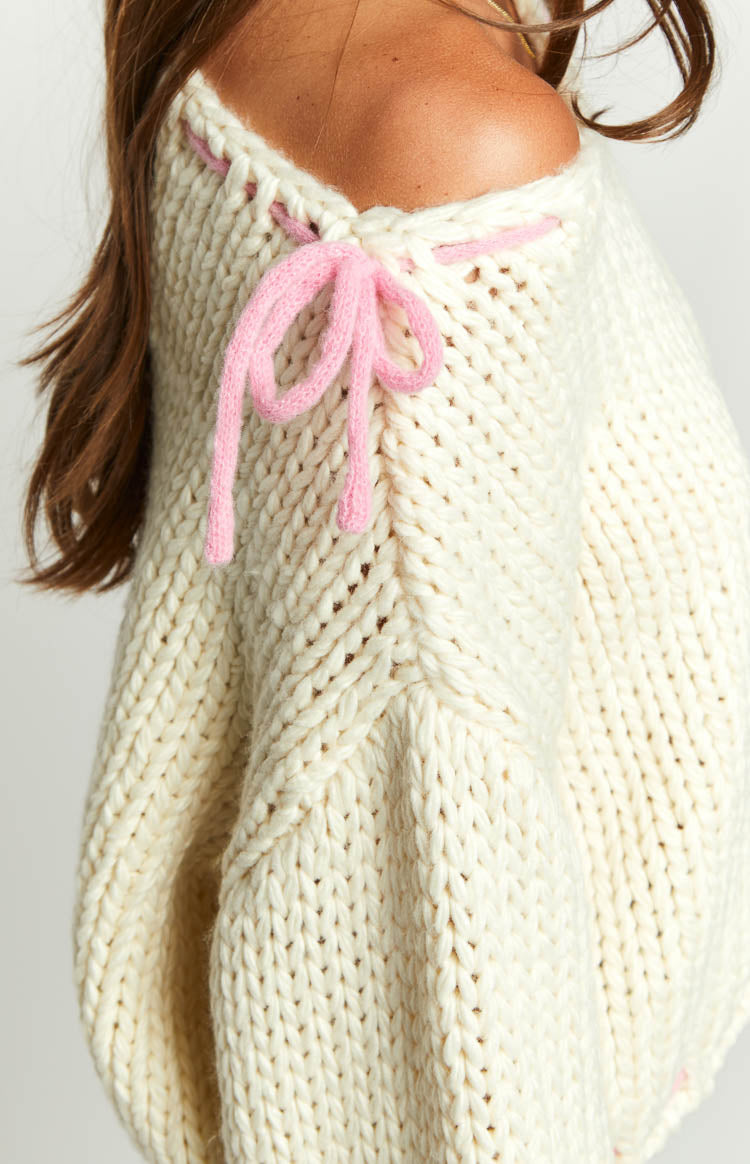 Close-up of the cream chunky knit sweater shoulder with pink lacing and a decorative bow