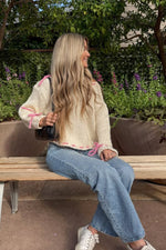 Side view of a cream chunky knit sweater with pink ribbon ties on the shoulders, cuffs, and hem