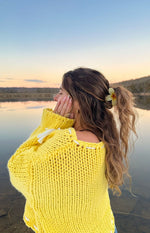 Side view of a chunky knit yellow sweater with white tie details on the shoulder and sleeve