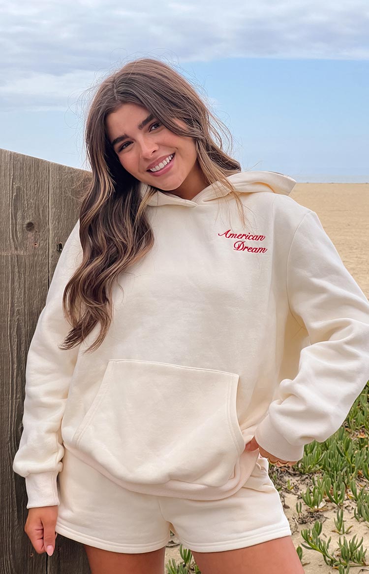 Close-up of the cream hoodie showing red American Dream embroidery and front kangaroo pocket