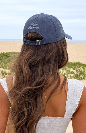 Girl wearing a washed blue dad cap with an adjustable head band and embroidered graphic text
