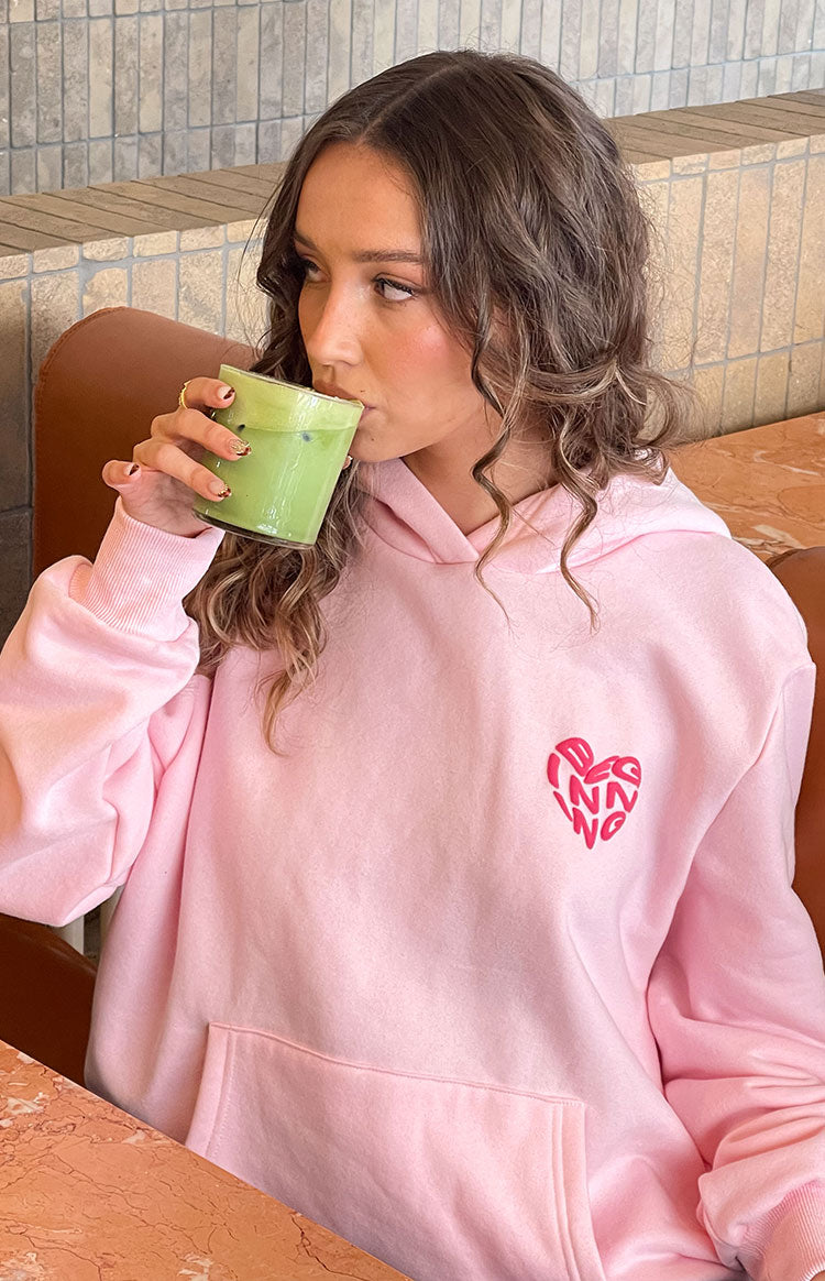 Pink hoodie with a red heart graphic on the chest, a front kangaroo pocket, and ribbed cuffs