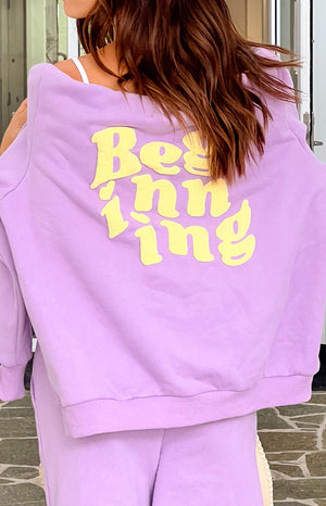 Rear view of a purple hoodie with yellow raised "Beginning" text on the back, worn off-shoulder