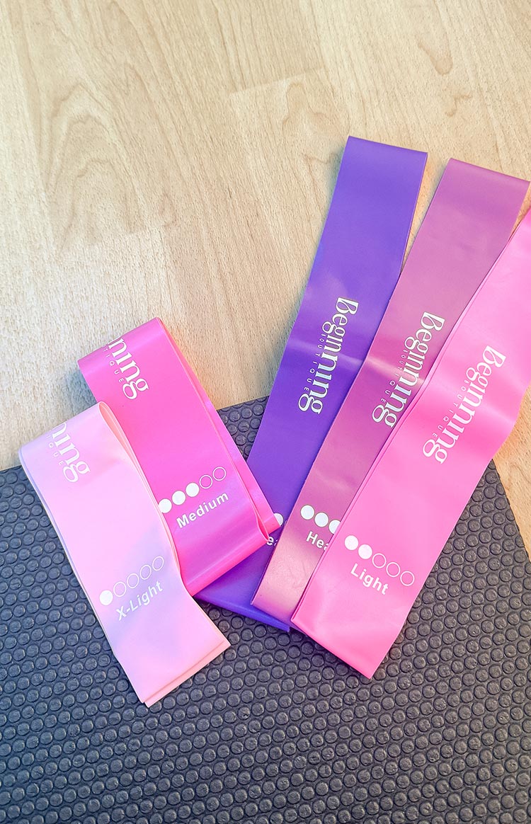 Assortment of light pink, hot pink, magenta, and purple resistance bands, displaying X-Light, Medium, Heavy, and Light levels