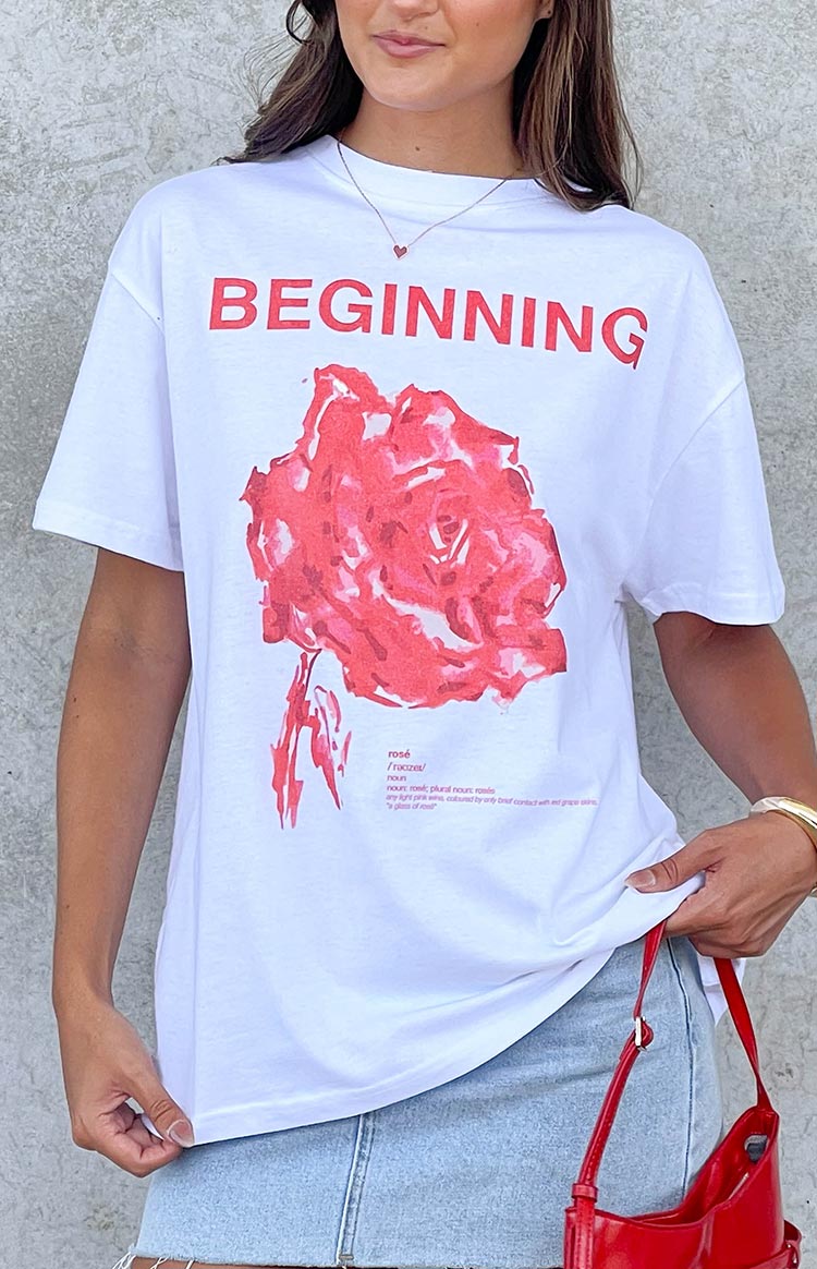 Detail of the white oversized tee featuring red BEGINNING text a pink rose graphic and rosé definition