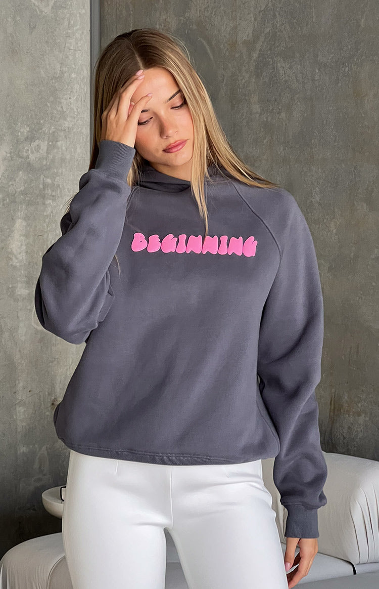 Close-up of the slate grey hoodie with pink bubble 'BEGINNING' text, raglan sleeves, and ribbed cuffs