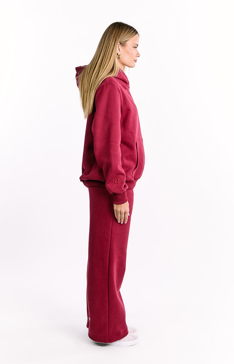 Side view of an oversized burgundy hoodie with a kangaroo pocket and embroidered logo on the sleeve