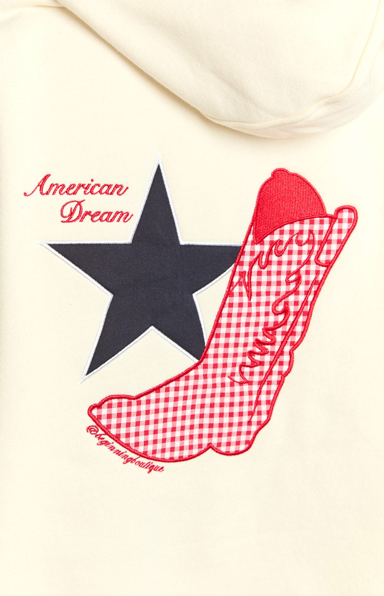 Close-up of the cream hoodie featuring a red American Dream text, black star, and red gingham cowboy boot graphic
