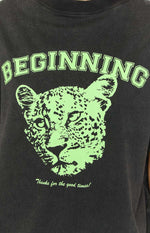 Close-up of the neon green graphic print on a washed black tee, featuring 'BEGINNING' text and a cub head design