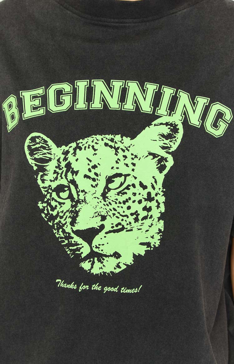 Close-up of the neon green graphic print on a washed black tee, featuring 'BEGINNING' text and a cub head design