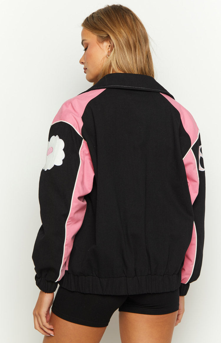 Rear view of a black bomber jacket with pink shoulder panels, white piping, and white flower and BB graphics