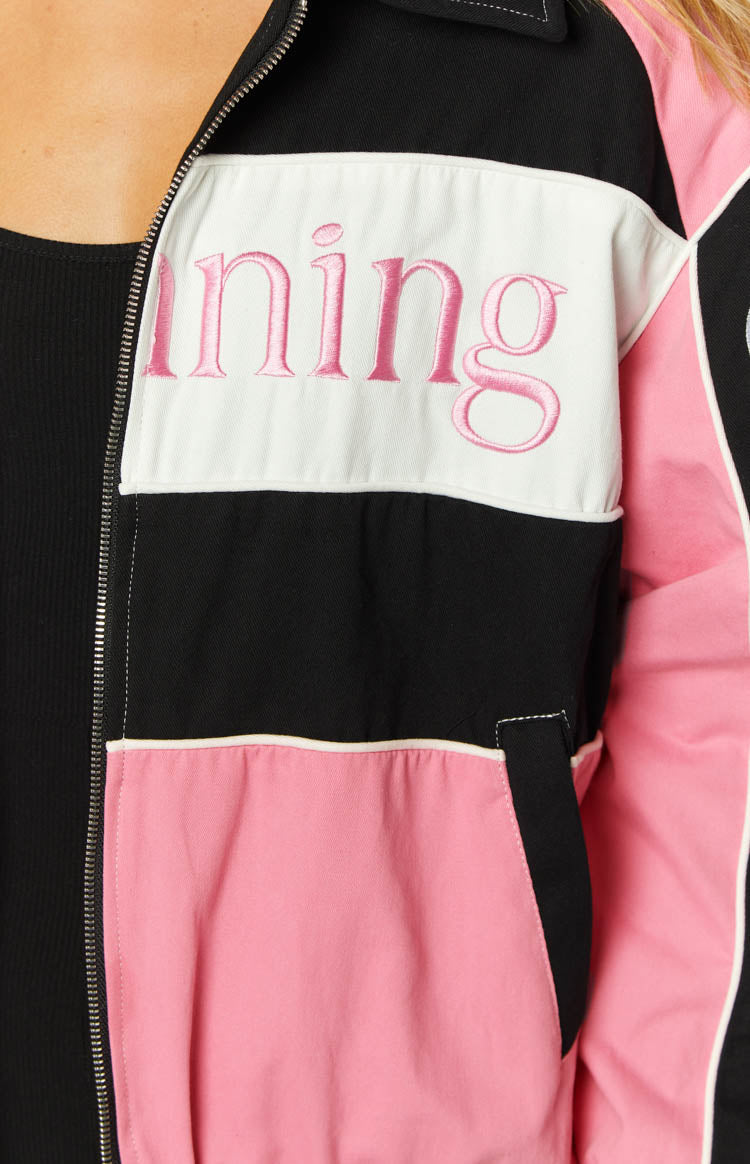 Close-up of the black, white, and pink colour-blocked bomber jacket showing pink embroidered text, silver zipper, and side pocket