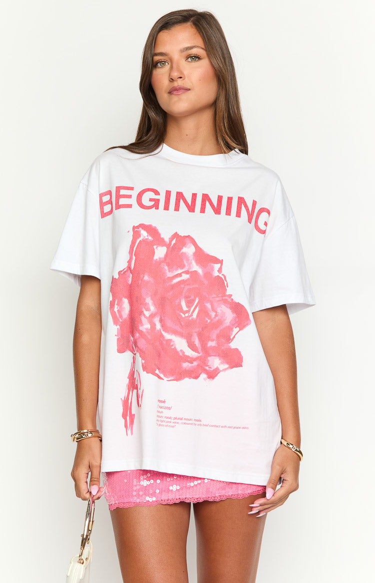 White oversized tee with a large pink rose graphic, BEGINNING text, and a small rosé definition print