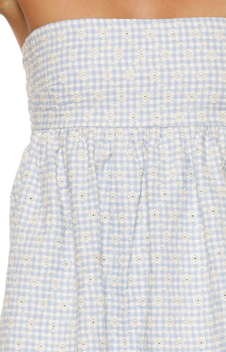 Close-up of the blue and white gingham fabric with white floral embroidery and gathered waist seam