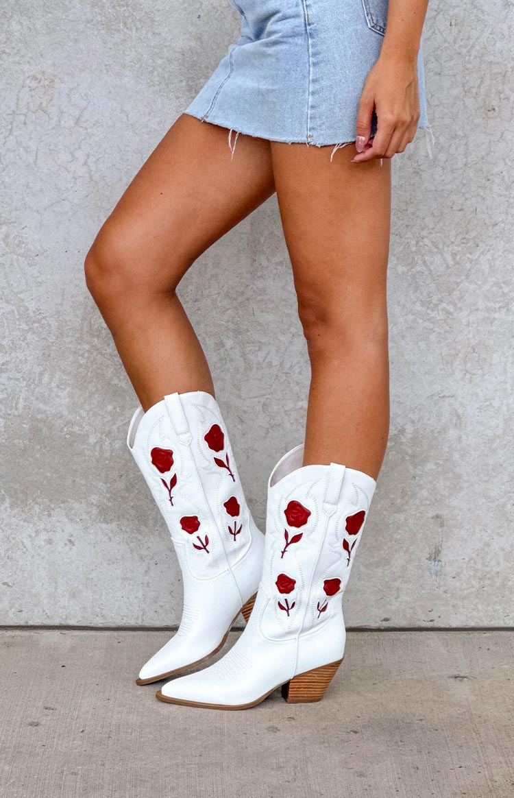 Side view of white cowboy boots with red rose embroidery, pointed toe, and stacked wooden heel
