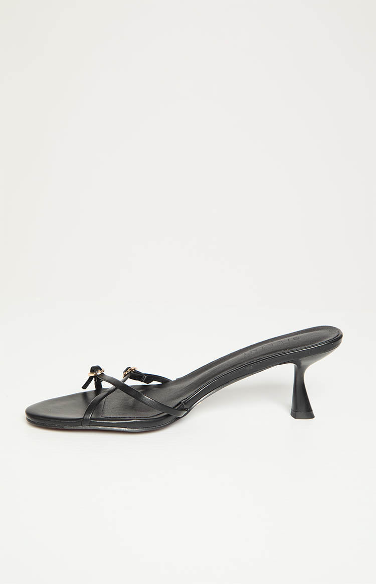 Side view of a black mule heel with thin straps, gold hardware, and a flared heel