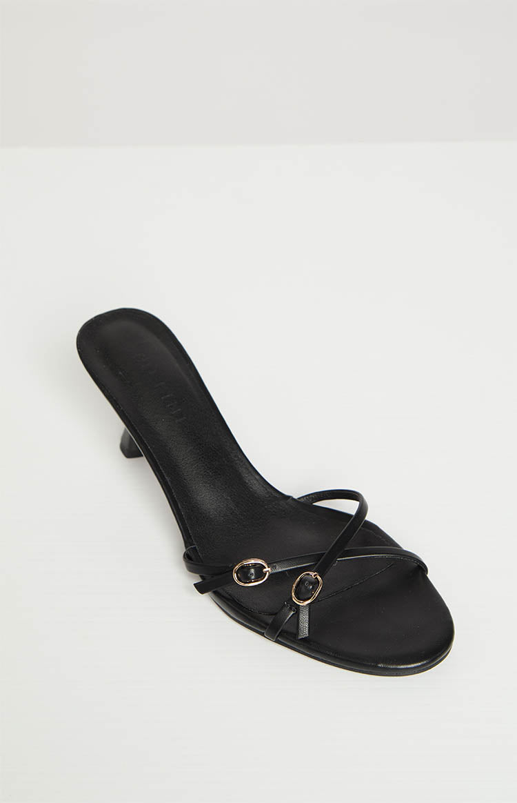 Close-up of the black strappy heels showing thin front straps with two small gold ring buckles