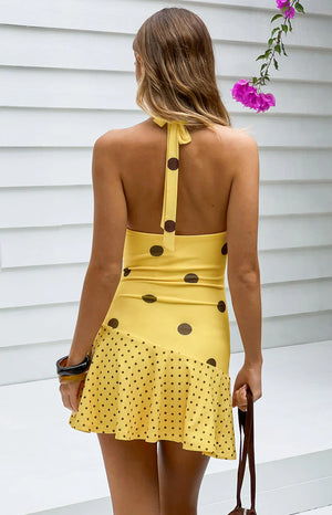Rear view of a yellow polka dot mini dress with a halter neck tie and open back The bodice has large dots, the skirt has smal