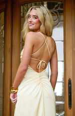 Rear view of a yellow satin maxi dress with criss-cross spaghetti straps, tie-back, and ruched detail