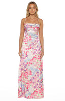 A full-length studio shot of our model wearing a floor-length satin-style maxi dress. This garment features an all-over vibrant floral print with pink purple and green blossoms on a light-colored background. It has thin spaghetti straps a straight-across neckline and a horizontally ruched bodice.