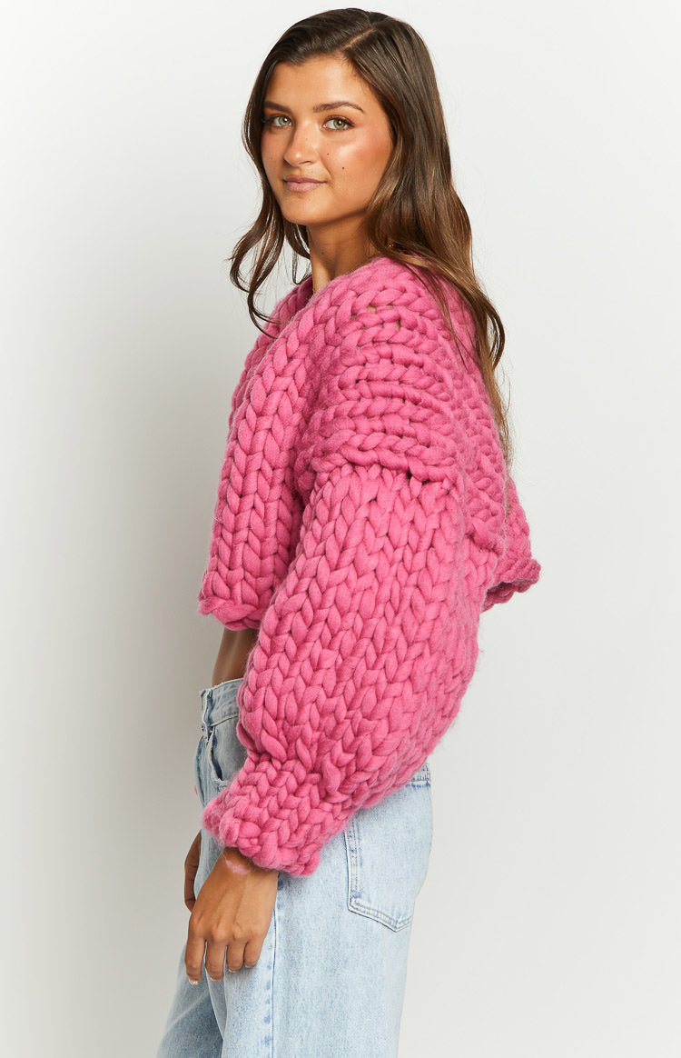 Side view of a bright pink chunky knit cardigan, showing its cropped length and voluminous long sleeves