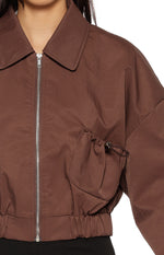 Close-up of the chocolate bomber jacket showing the drawstring detail on the front and elasticated hem
