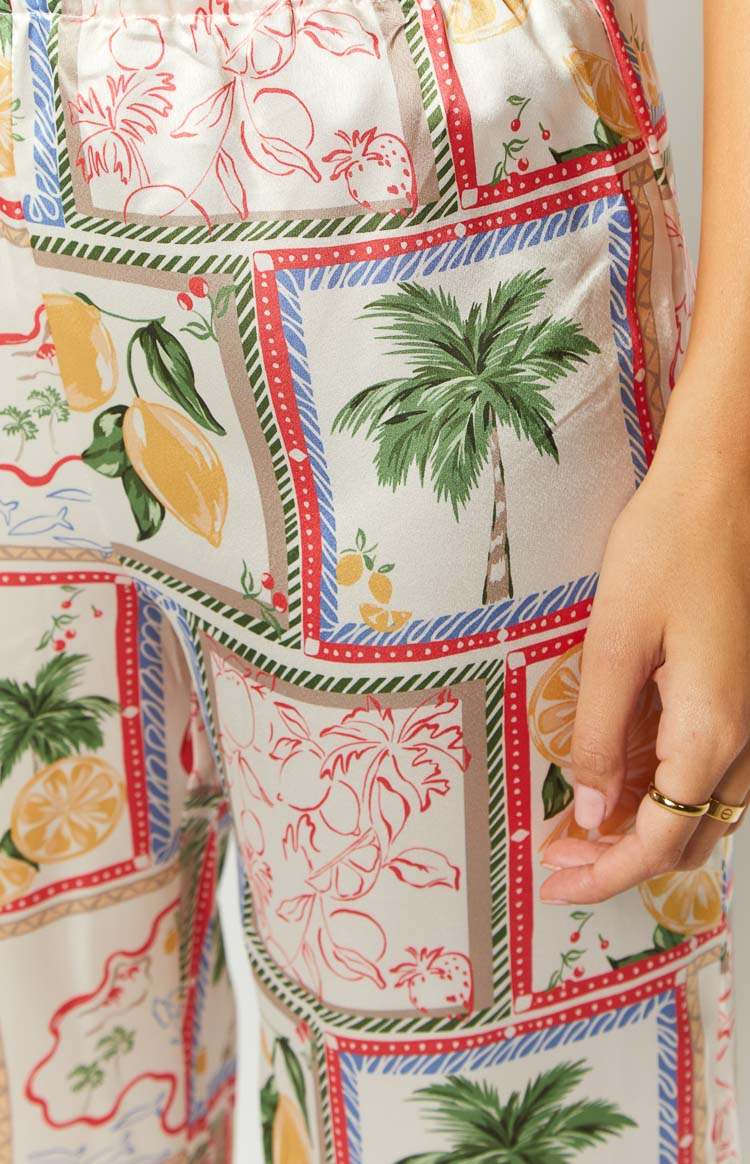 Side view showing the full length and flowy drape of the white satin wide-leg pants with a colorful square-patterned Roma print