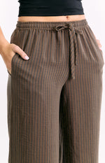 Close-up of the elasticated drawstring waistband with a tie knot and side pockets of brown striped pants