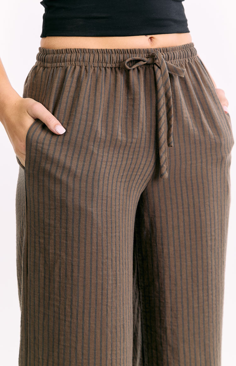 Close-up of the elasticated drawstring waistband with a tie knot and side pockets of brown striped pants