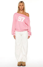 Front view of a pink wash off shoulder sweater with white '97' graphic and long cuffed sleeves