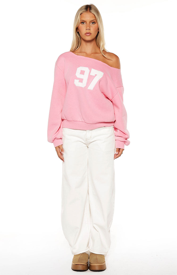 Front view of a pink wash off shoulder sweater with white '97' graphic and long cuffed sleeves