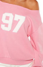 Close-up of the pink off-shoulder sweater showing the white '97' graphic and raw edge neckline