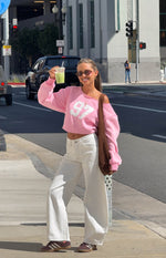 Front view of a pink off-shoulder cropped sweater featuring a large white '97' graphic on the chest