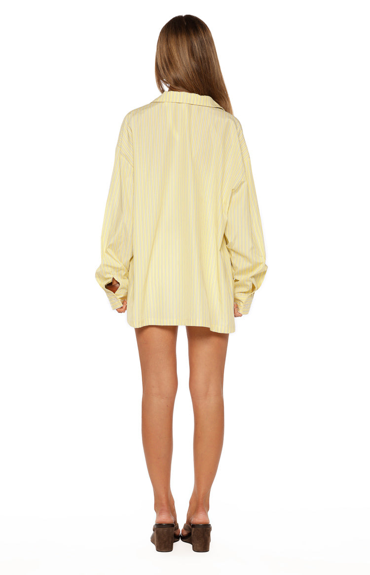 Rear view of an oversized yellow and white striped long sleeve button-up shirt with a collared neckline