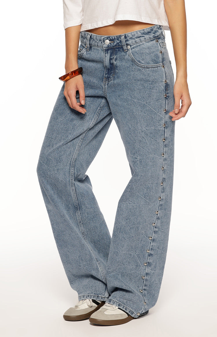 Side view of mid wash denim baggy leg jeans with silver studs running down the outer seams