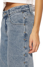 Side view of mid-wash denim jeans with silver stud details along the outer seam and a front pocket