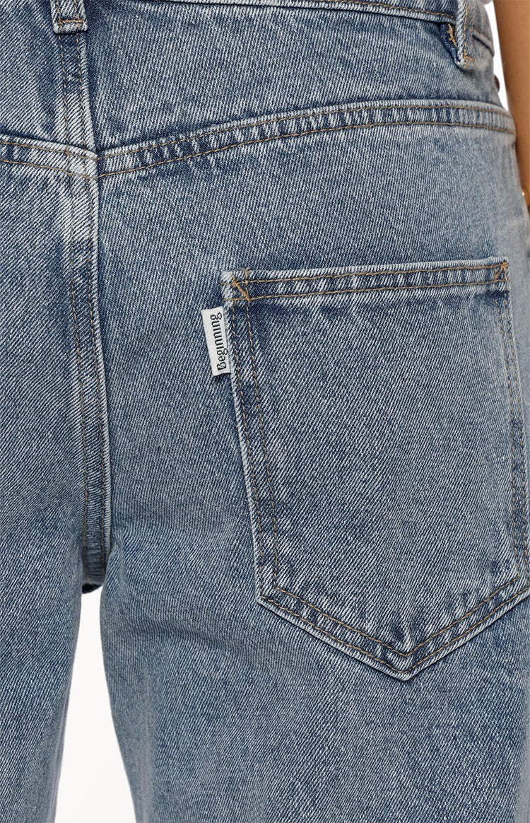 Close-up of the back pocket on mid-wash denim jeans with tan contrast stitching and a small white tag