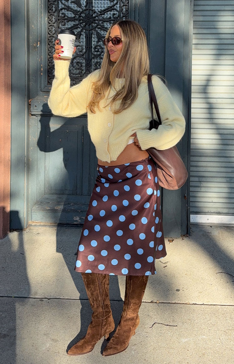 Angled front view of a brown midi skirt with large blue polka dots, showing its flowy satin-like drape