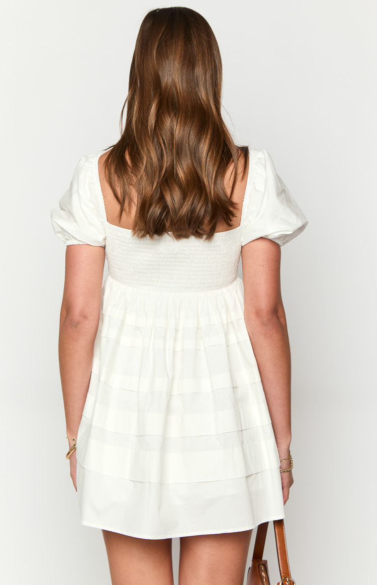 Back view of a white babydoll mini dress with a square neckline, shirred back, puff sleeves, and tiered skirt