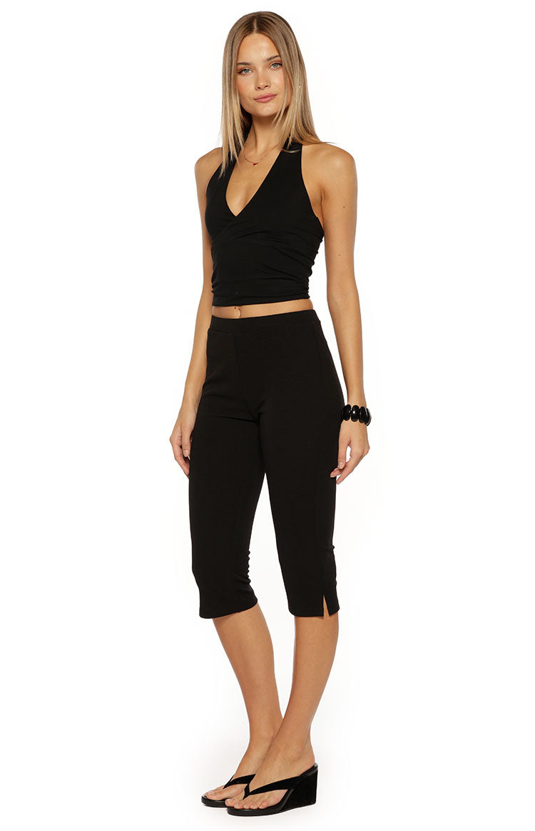 Side view of black jersey capri pants, showing the fitted silhouette, mid-calf length, and small slits at the outer hem