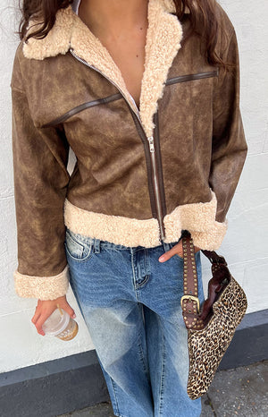 Close-up of a brown distressed faux leather aviator jacket with cream faux shearling trim at the collar, cuffs, and hem