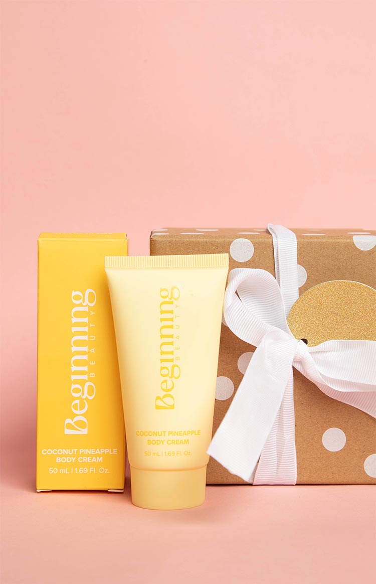 Yellow body cream tube and matching box next to a brown polka dot gift box with white ribbon