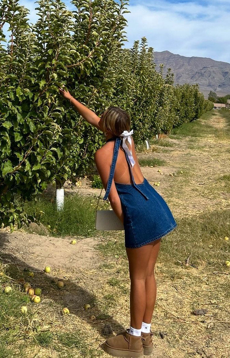 Rear view of a blue denim halter neck mini dress with an open back and tie detail