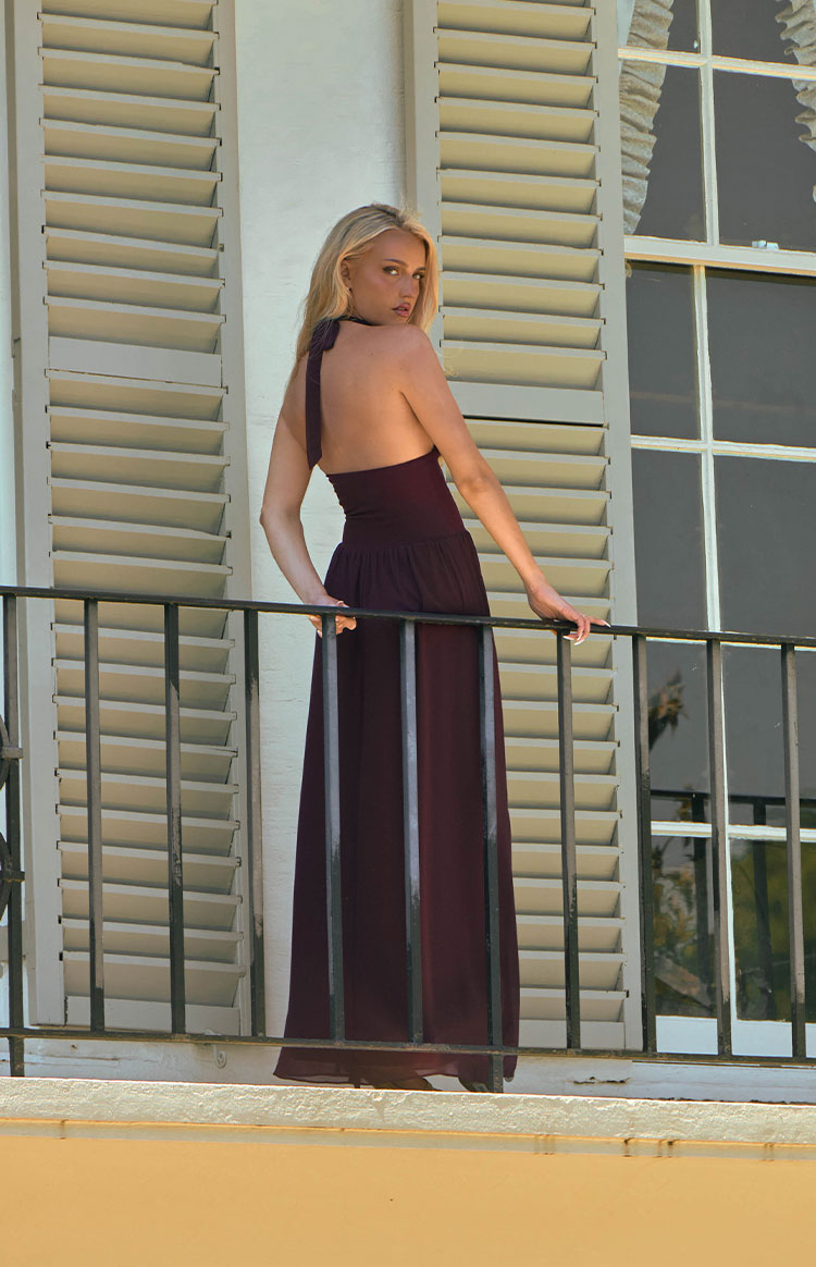 Rear view of a burgundy halter neck maxi dress with a tied back and gathered waist