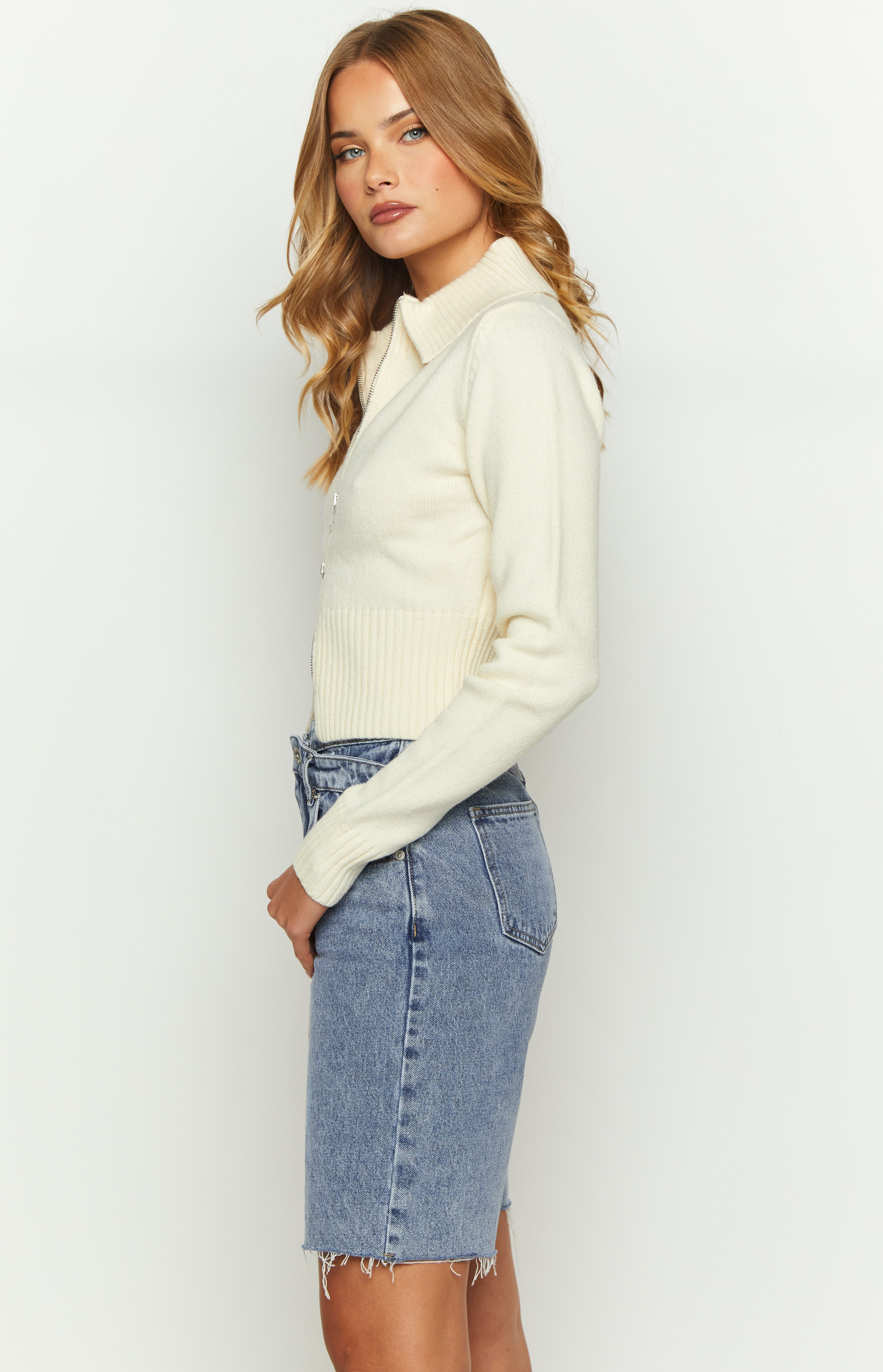 Side view of a cream collared sweater with a silver half-zip and ribbed hem