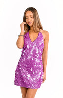 Rear view of our model wearing a vibrant purple mini dress with large all-over sequins. The dress has an open back with a tie closure at the neck.