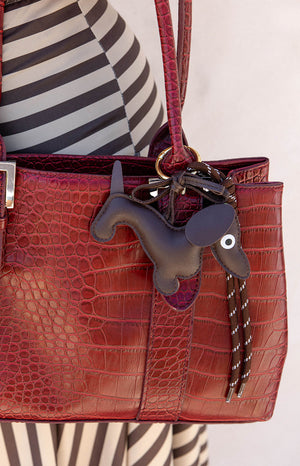 A gold dachshund shaped bag charm with a braided tan strap. This cute accessory features a clasp to attach to a handbag or keys. A perfect novelty gift for a dog lover or a fun addition to a casual outfit.