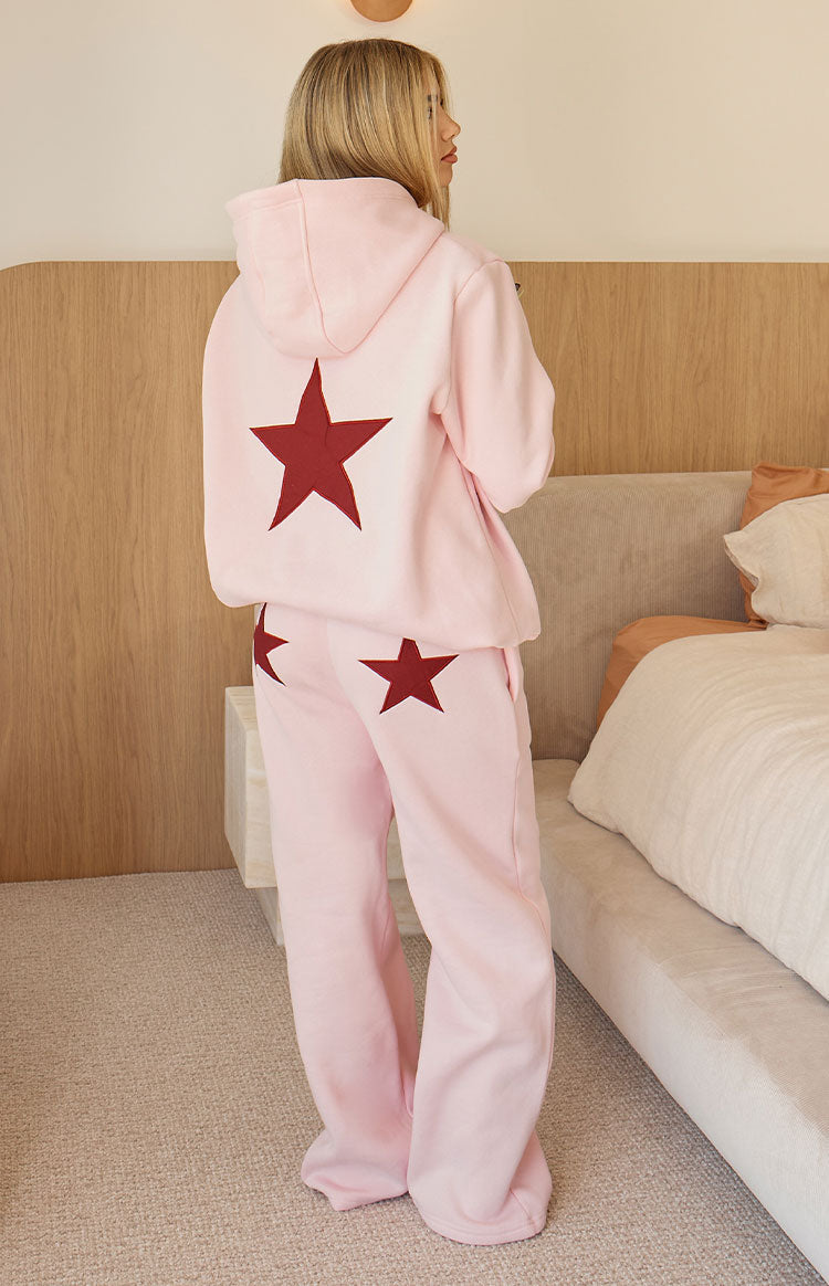 Back view of a light pink oversized hoodie with a large burgundy star and matching wide leg track pants with two stars
